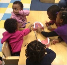 BBI toddlers practice brushing teeth the correct way using an interactive dental toy.